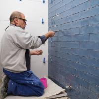 Senior murer arbejder på knæ på badeværelsesvæg